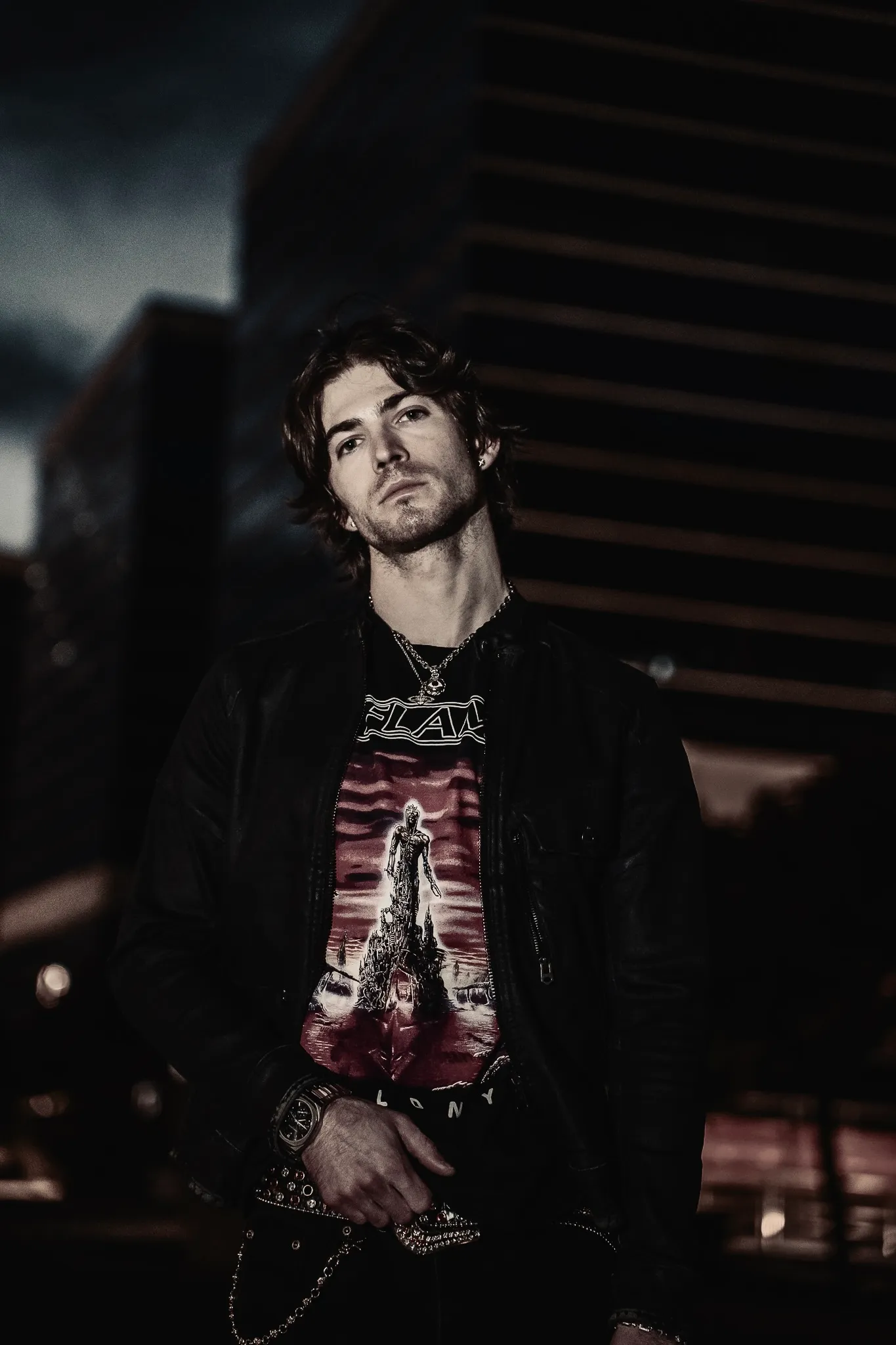 Portrait of Red Dot in a leather jacket against night-time city towers
